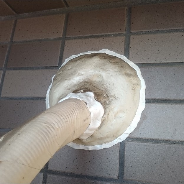 すきまパテで屋外のエアコン配管の隙間を塞ぐ様子